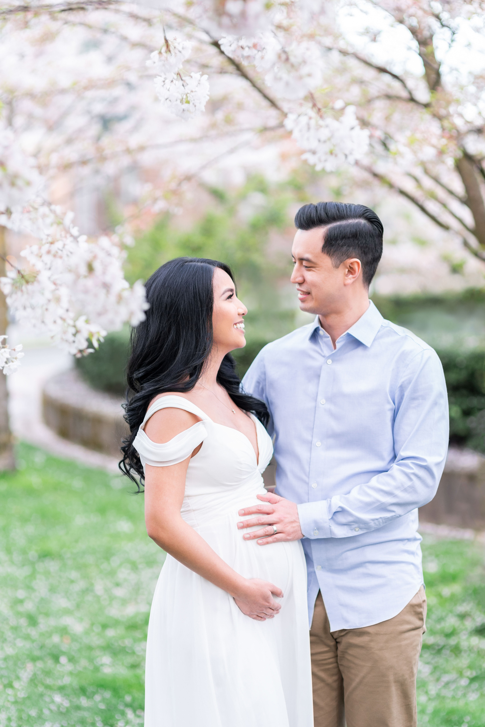 Cute pregnant Asian couple laughing in a cherry blossom park